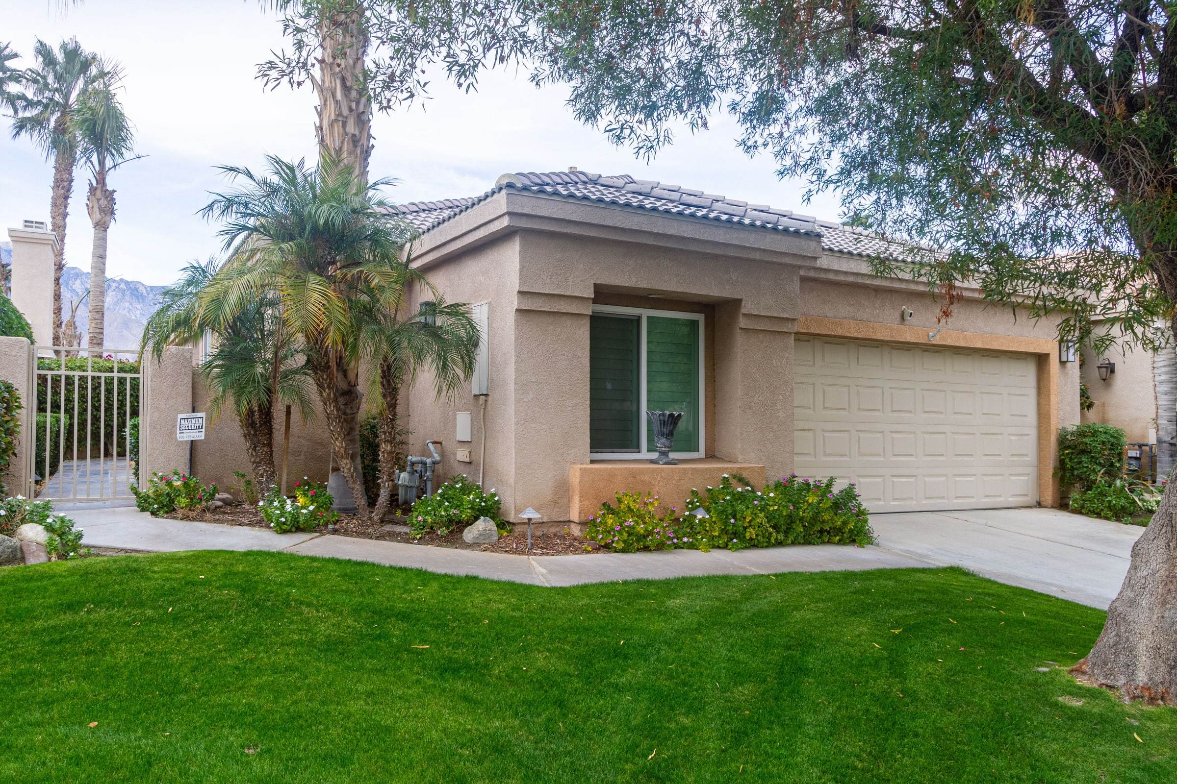 Front of the single-story house behind a lawn and palms, with the garage, the side gate and the mountains beyond