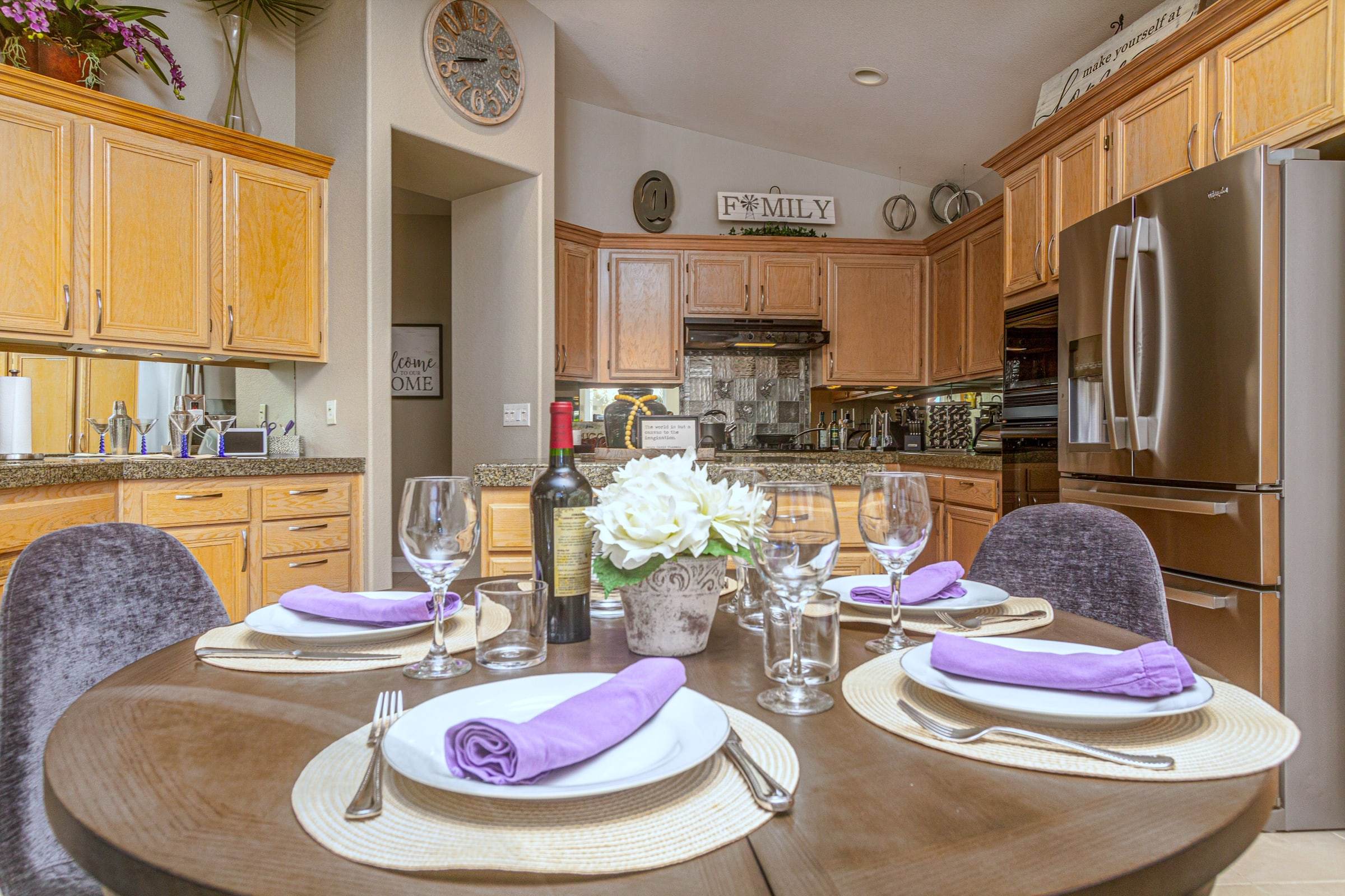 Dining nook table set for four with wine and white flowers, with the kitchen behind