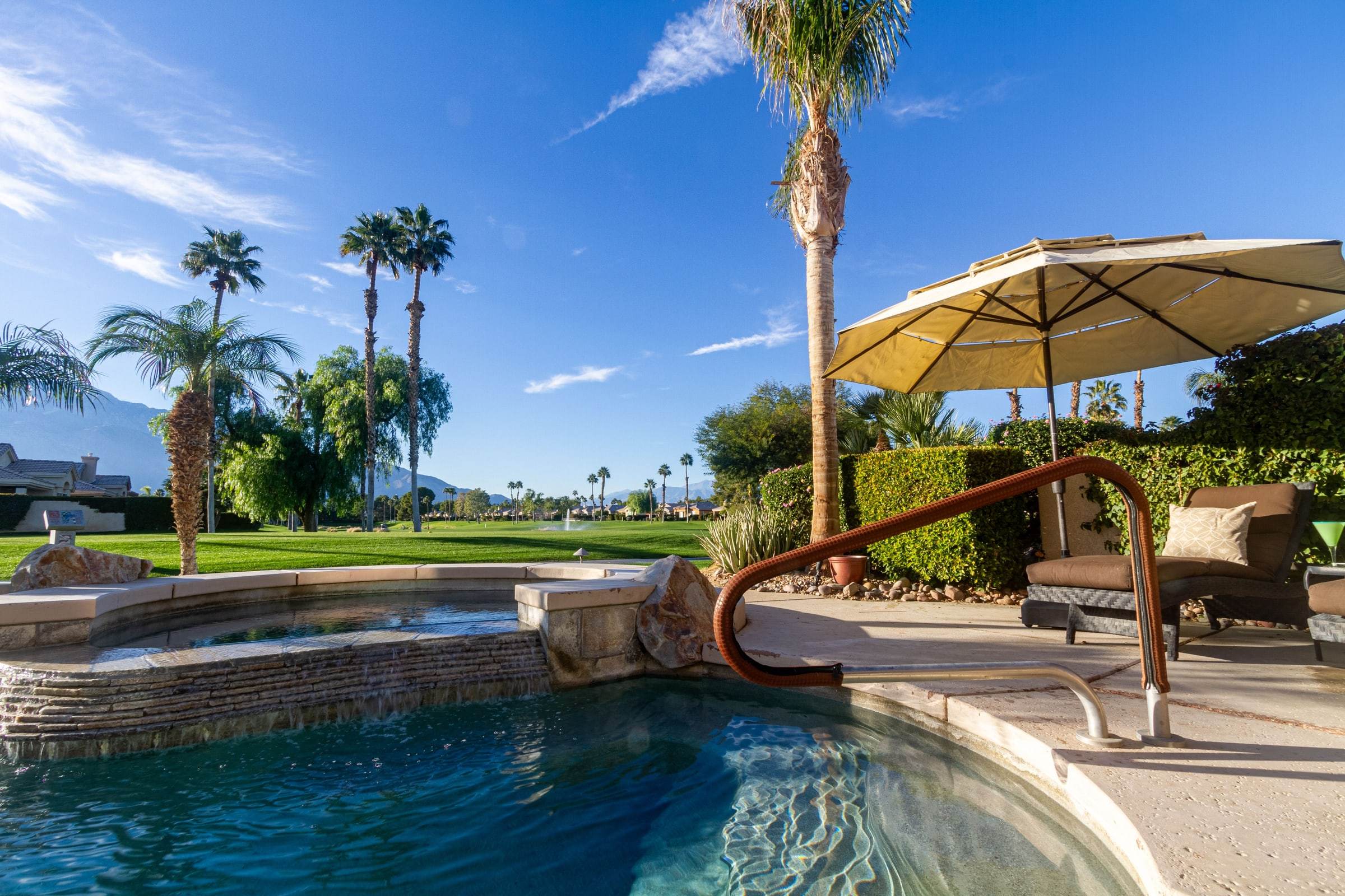 Spa spilling into the pool, with a handrail, an umbrella and the golf green behind